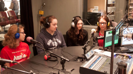 Four youth wearing headphones speaking into microphones in a radio studio