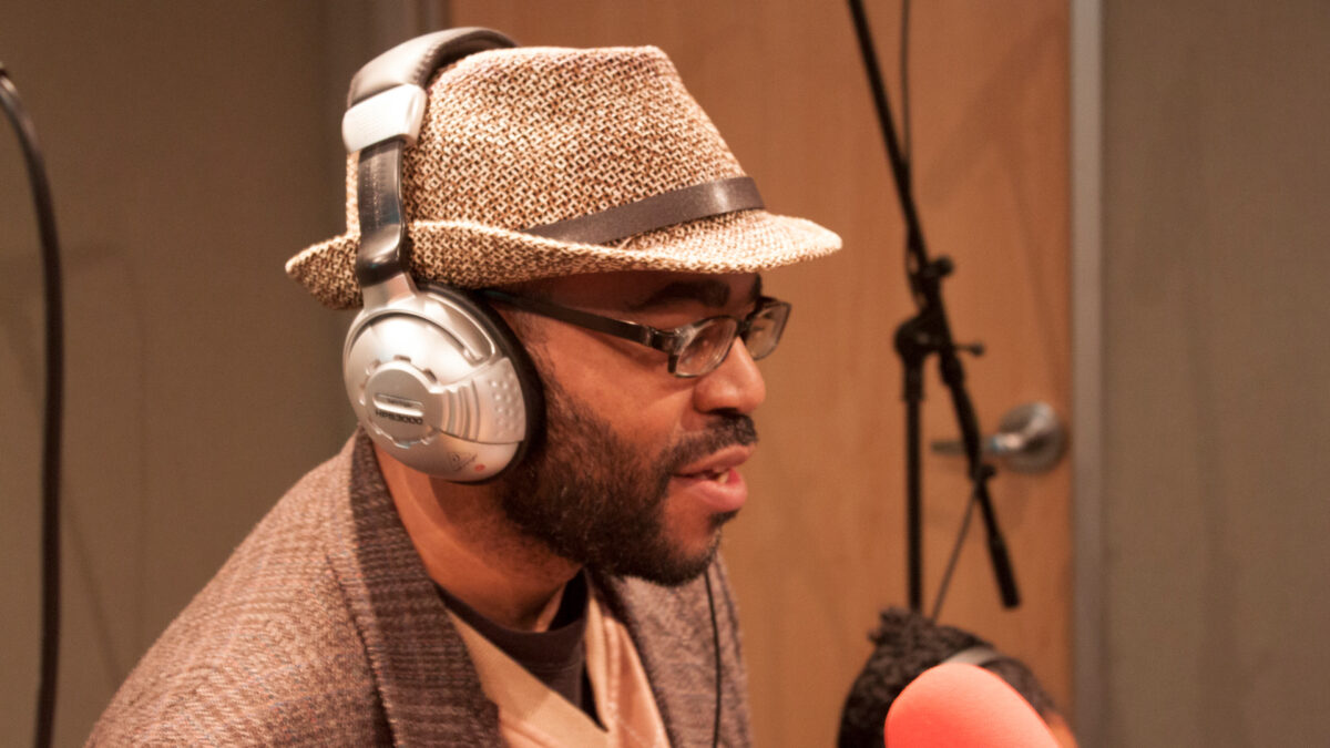 An adult wearing headphones singing into a microphone in a radio studio