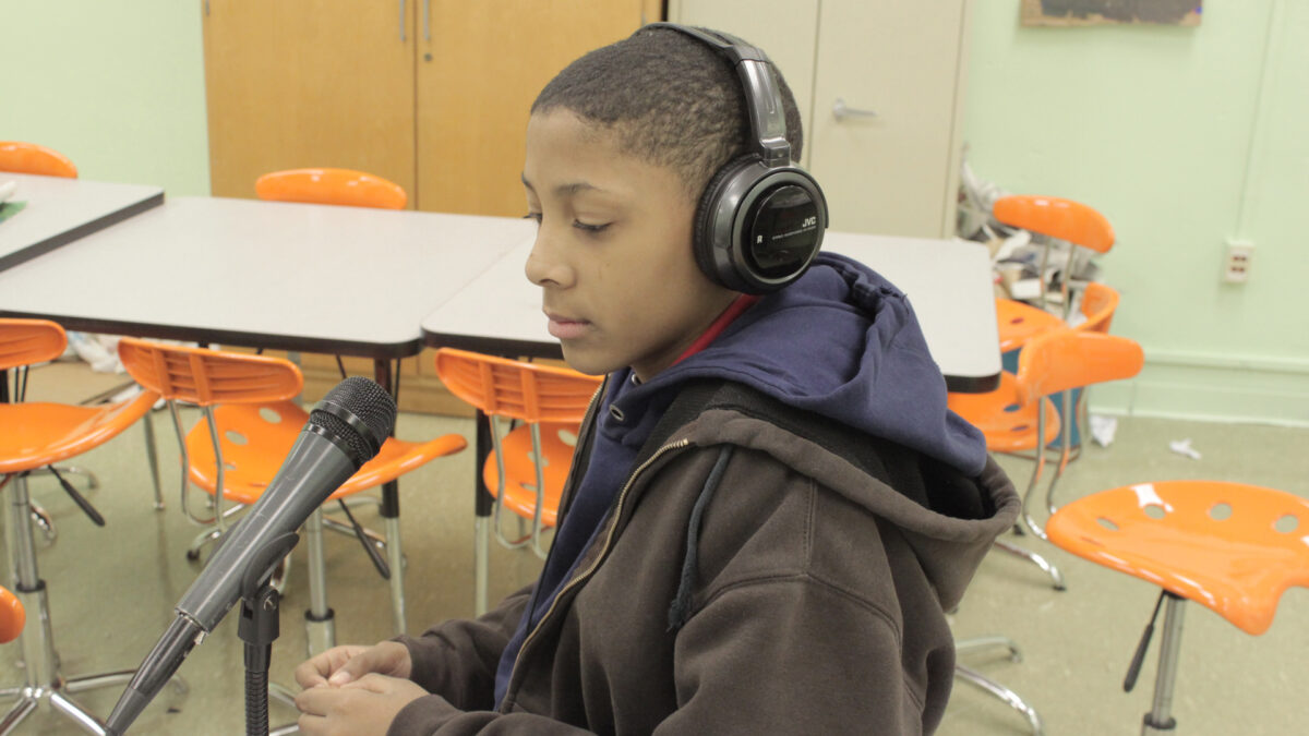 A youth wearing headphones sitting behind a microphone in a classroom