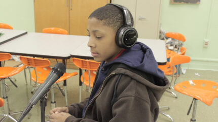 A youth wearing headphones sitting behind a microphone in a classroom