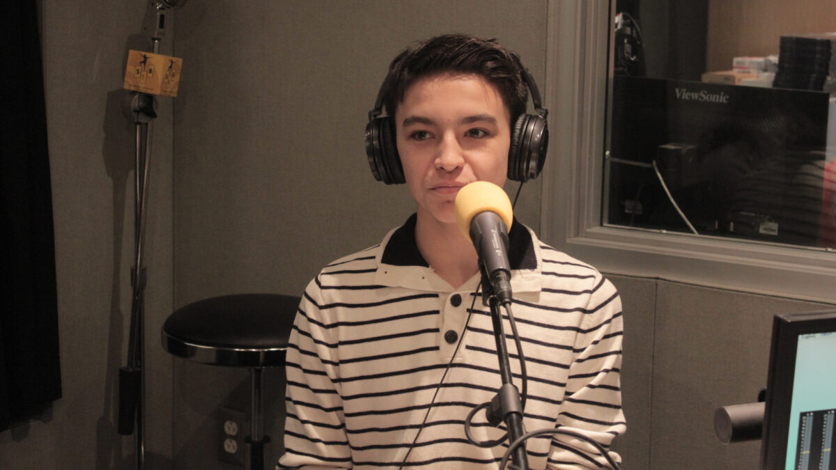 A teen wearing headphones sitting behind a microphone in a radio studio