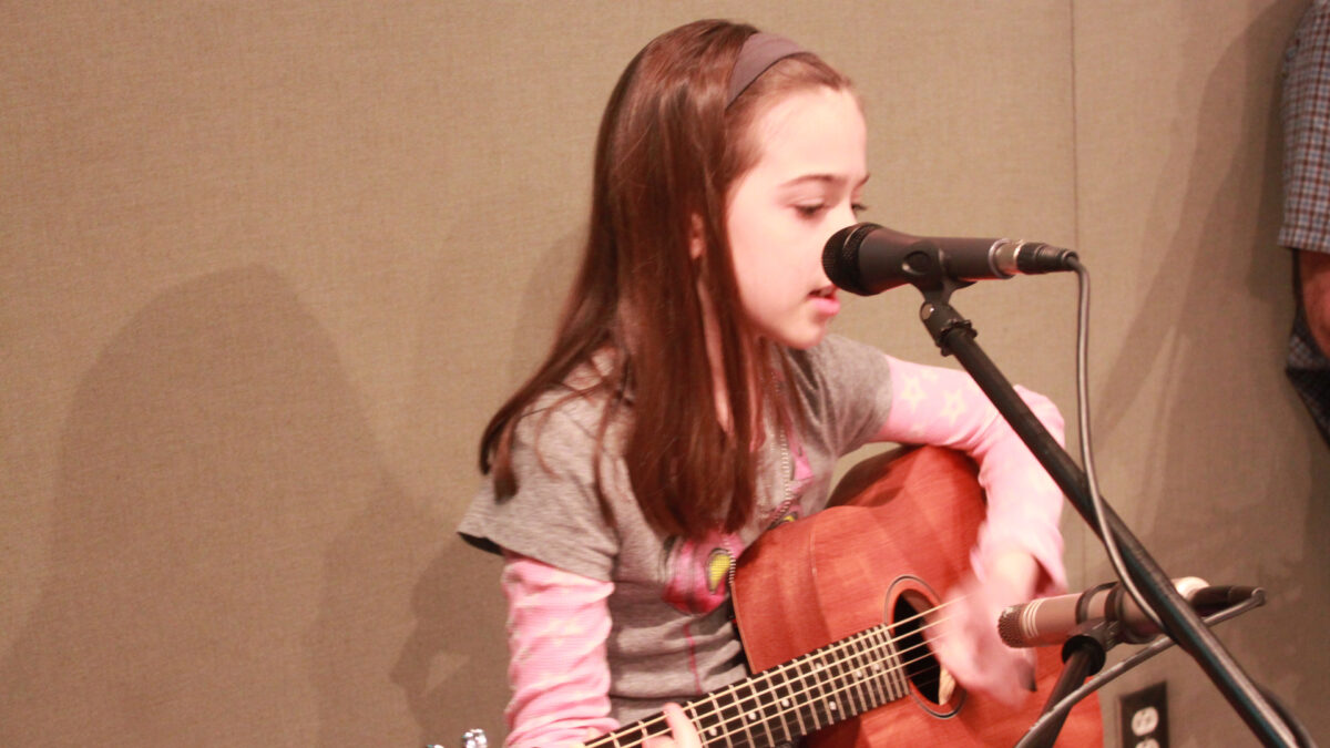 A youth playing an acoustic guitar and singing into a microphone in a radio studio