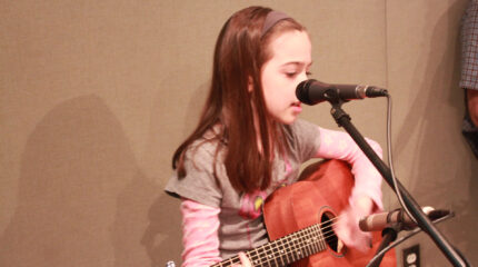 A youth playing an acoustic guitar and singing into a microphone in a radio studio