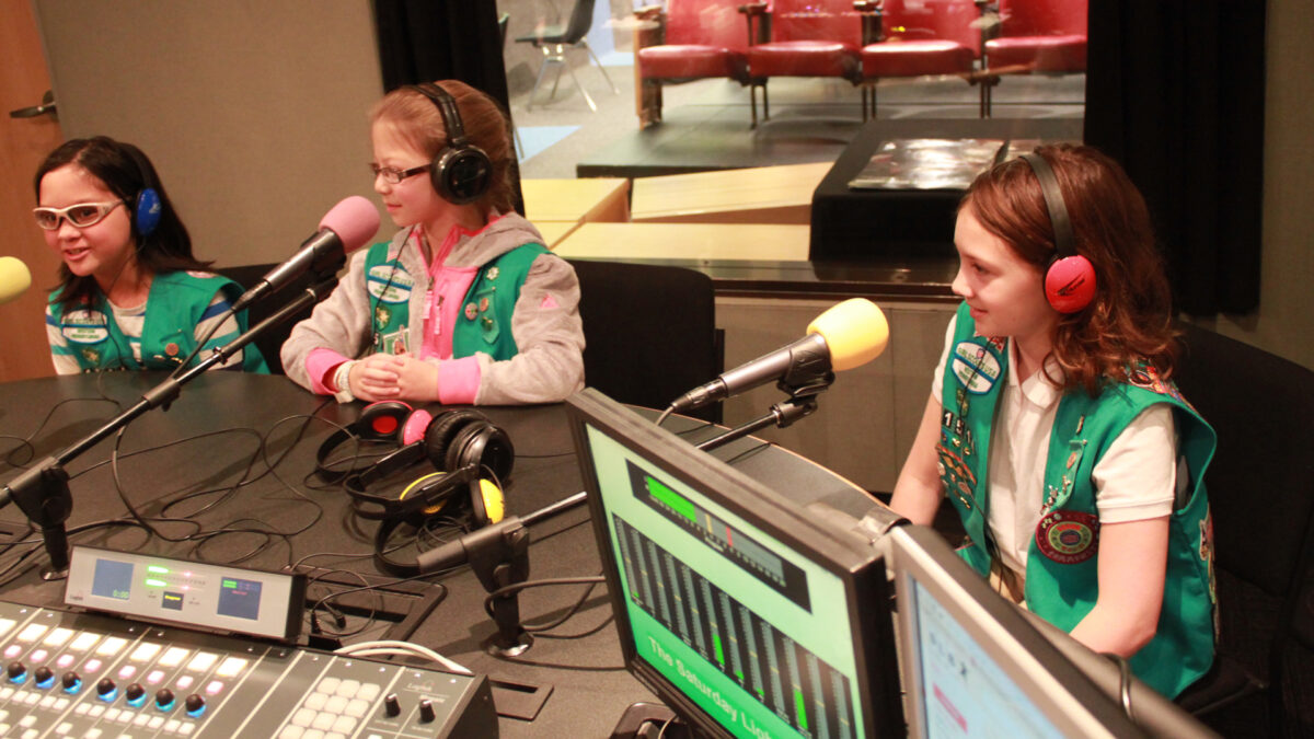 Three youth wearing headphones speaking into microphones in a radio studio