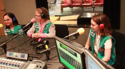 Three youth wearing headphones speaking into microphones in a radio studio