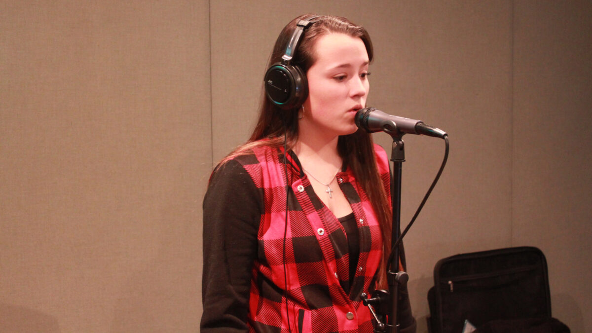 A teen wearing headphones singing into a microphone in a radio studio