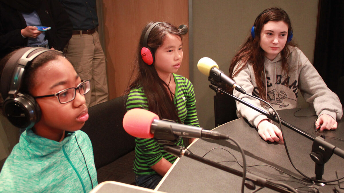 Three youth wearing headphones speaking into microphones in a radio studio