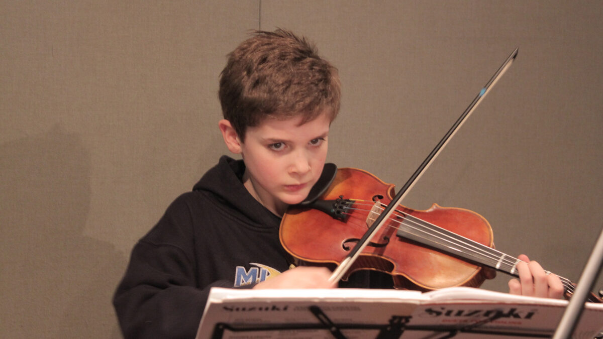 A youth playing a violin looking at sheet music on a music stand in a radio studio
