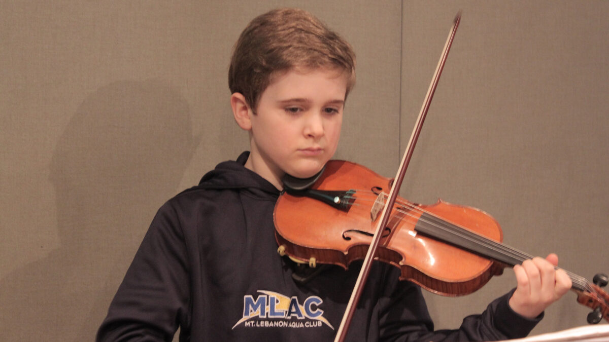 A youth playing a violin looking at sheet music on a music stand in a radio studio