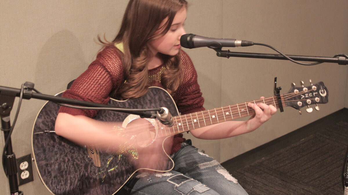 A youth playing an acoustic guitar and singing into a microphone in a radio studio