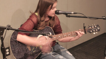 A youth playing an acoustic guitar and singing into a microphone in a radio studio