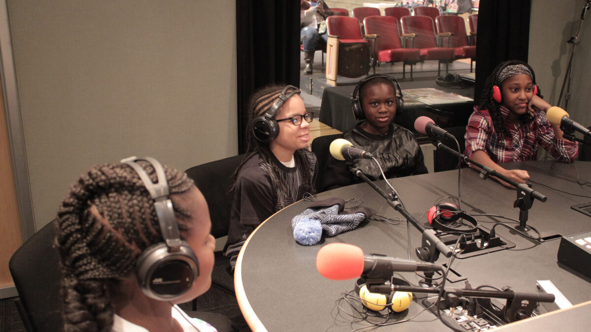 Four youth wearing headphones speaking into microphones in a radio studio