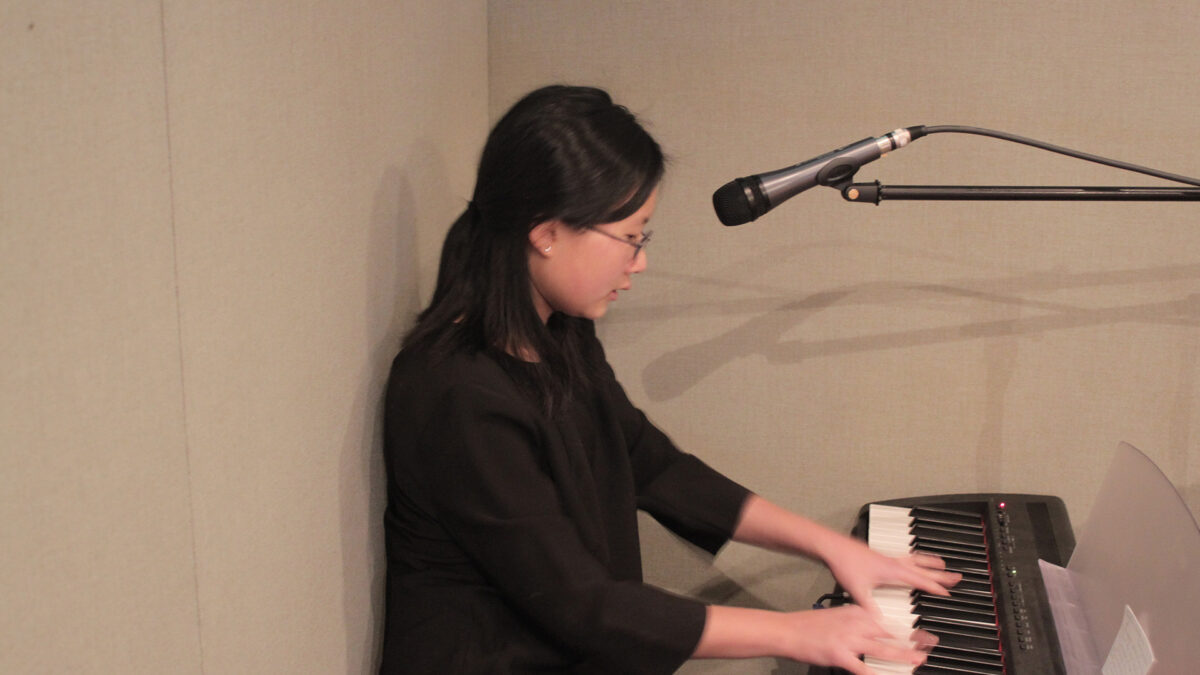 A teen playing a piano keyboard sitting behind a microphone in a radio studio