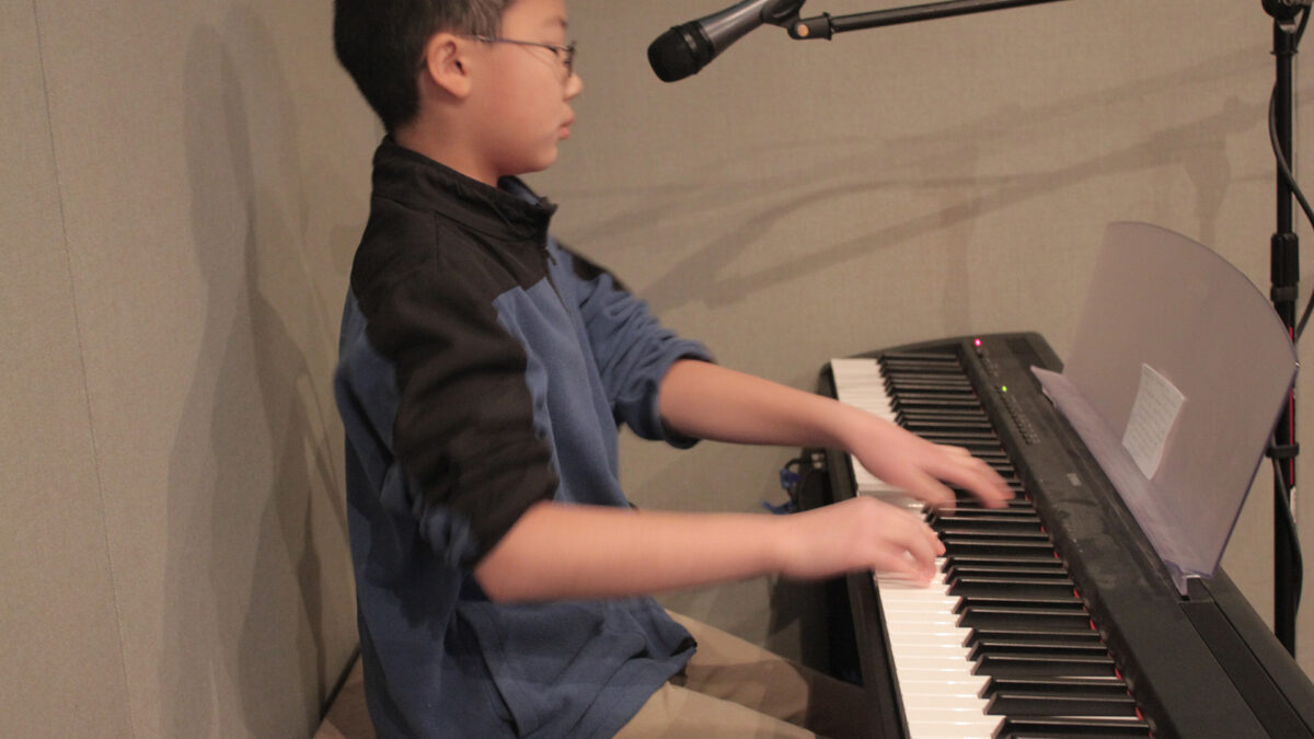 A child sitting behind a microphone playing a piano keyboard