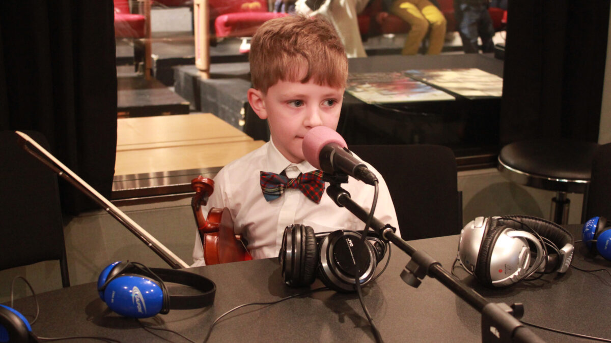A youth holding a microphone sitting behind a microphone in a radio studio