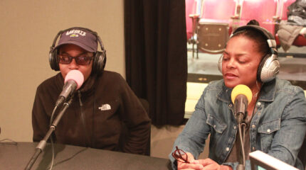 A teen and an adult wearing headphones speaking into microphones in a radio studio
