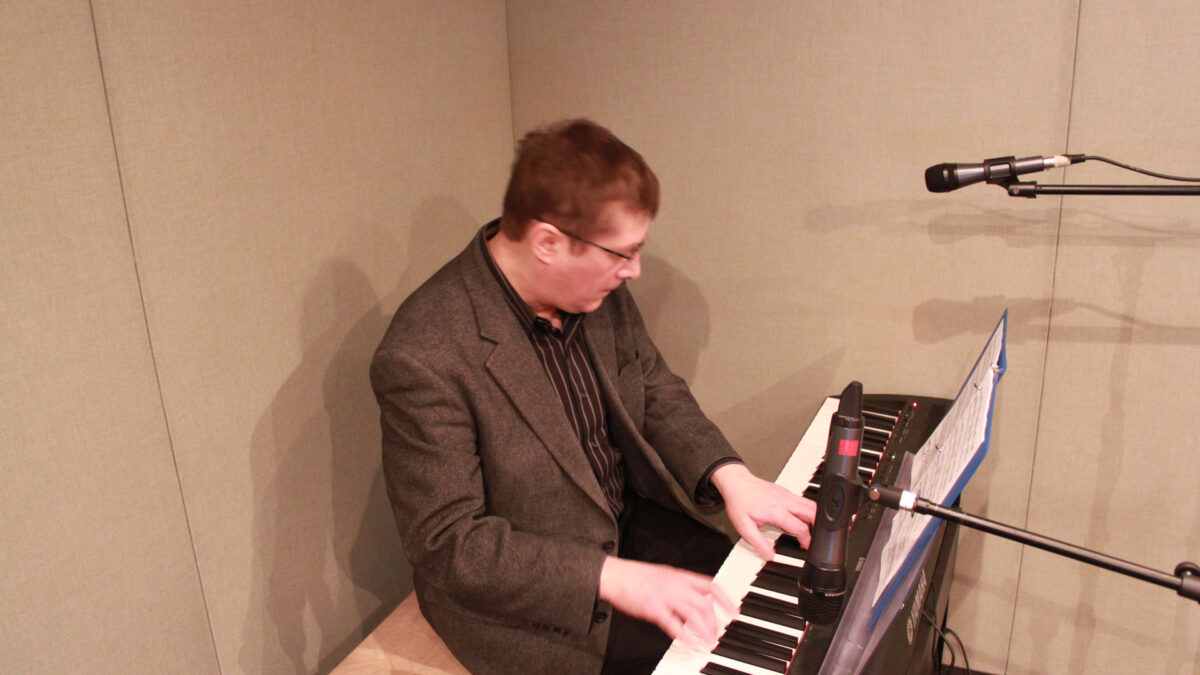 An adult playing a piano keyboard sitting behind a microphone in a radio studio