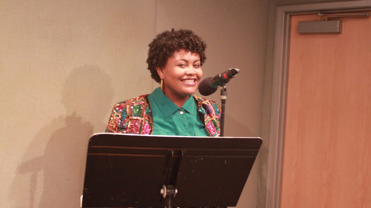A teen smiling standing behind a microphone and a music stand in a radio studio
