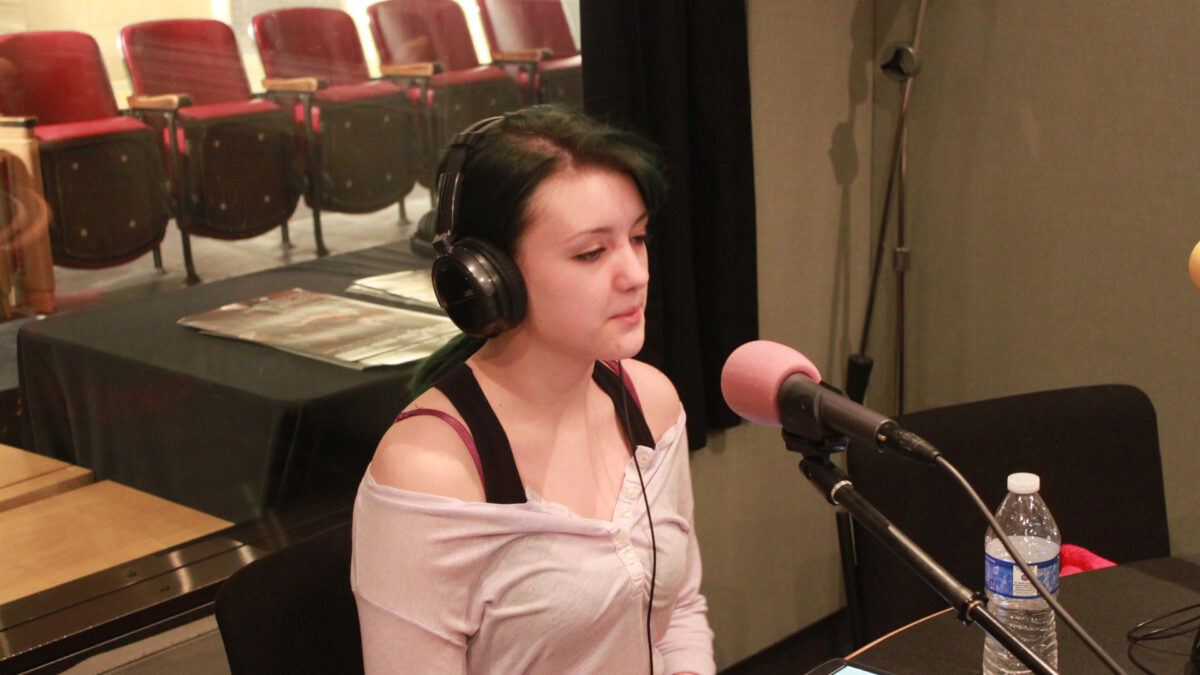 A teen wearing headphones speaking into a microphone in a radio studio