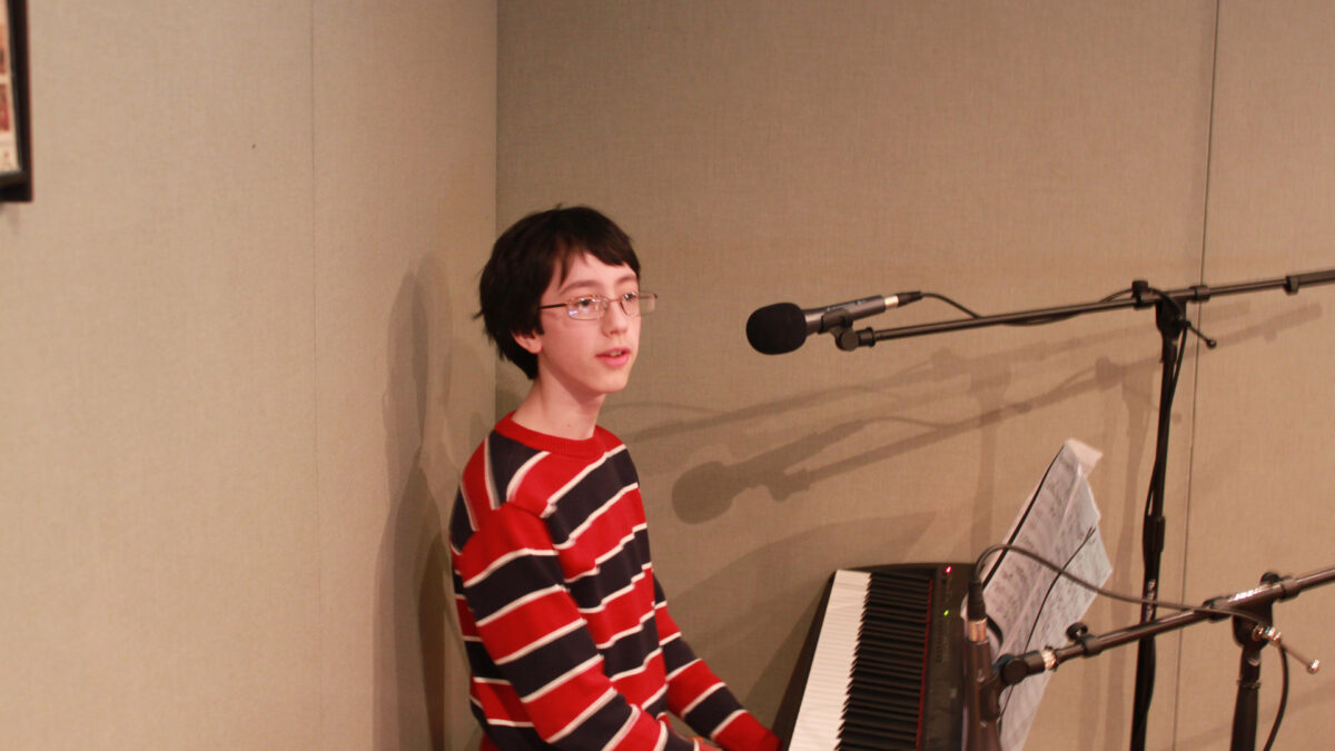 A youth sitting behind a piano keyboard and a microphone in a radio studio