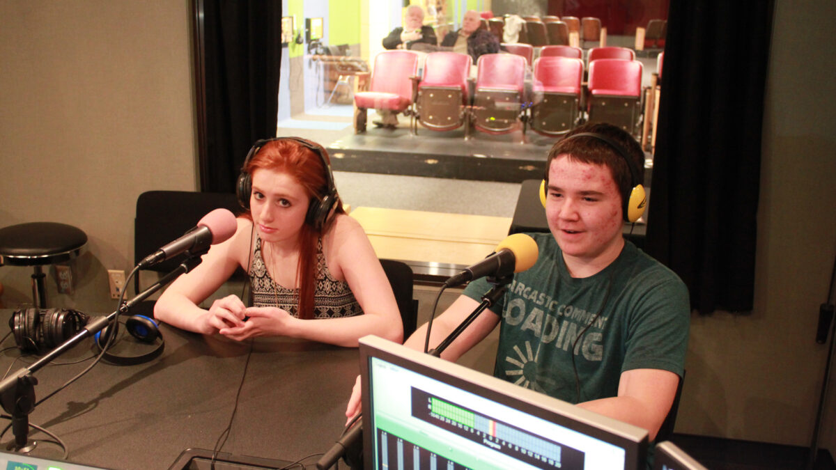 Two teens wearing headphones speaking into microphones in a radio studio