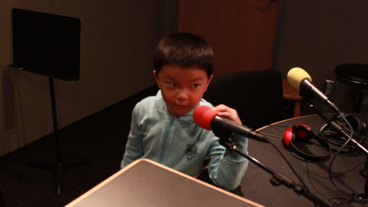 A youth sitting behind a microphone in a radio studio