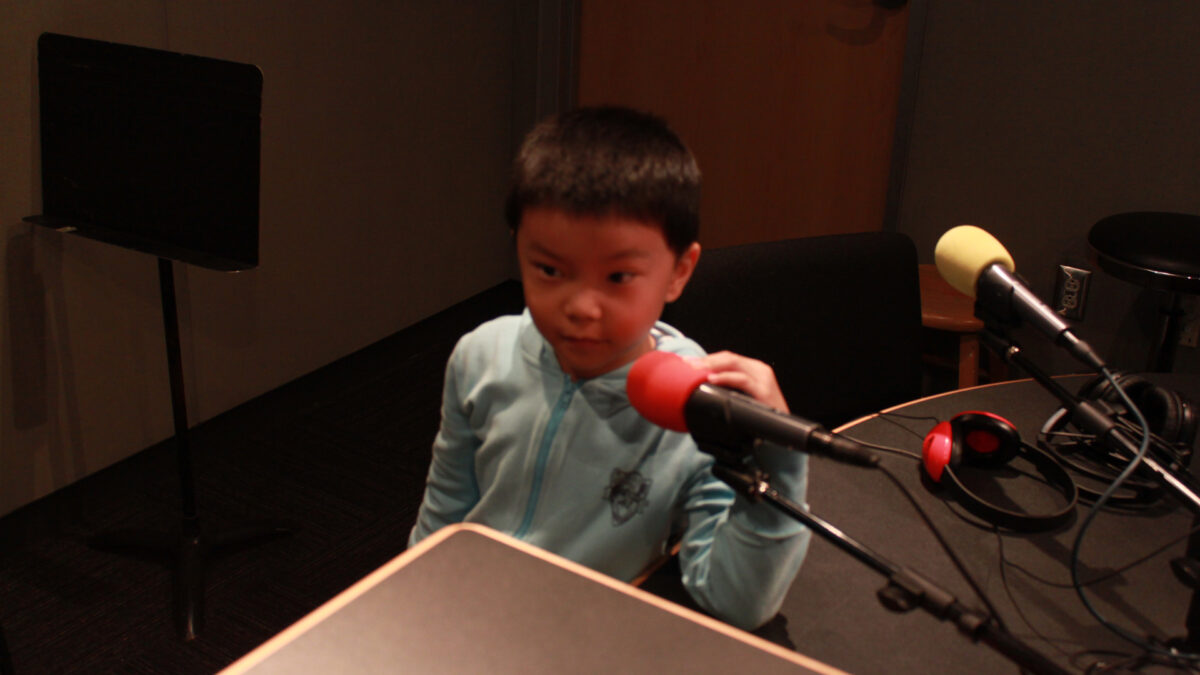 A youth sitting behind a microphone in a radio studio