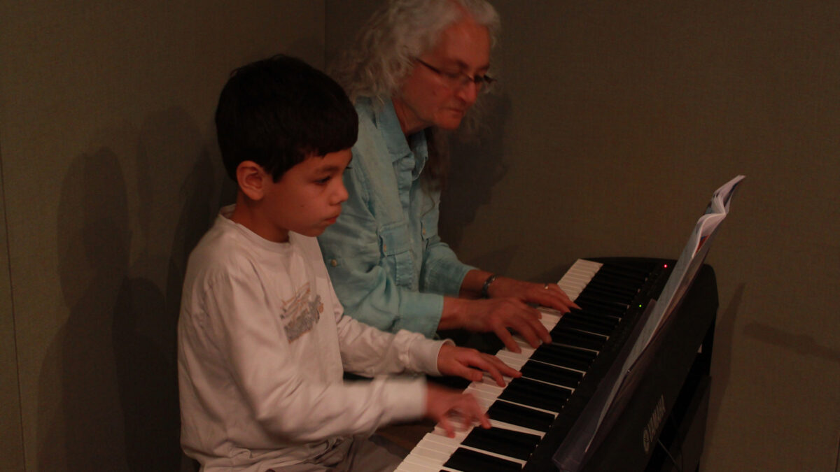 A youth and an adult playing a piano keyboard in a radio studio