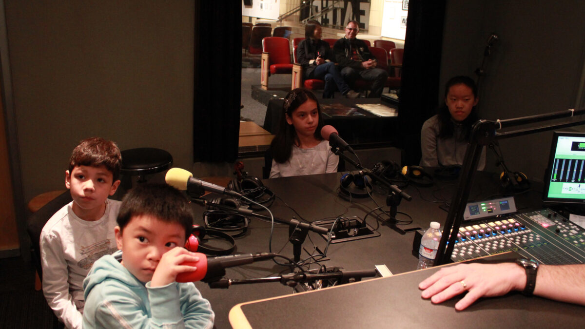 Four youth sitting behind microphones in a radio studio