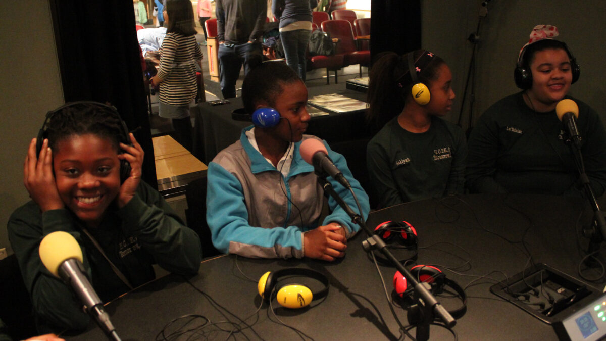 Four youths wearing headphones speaking into microphones in a radio studio