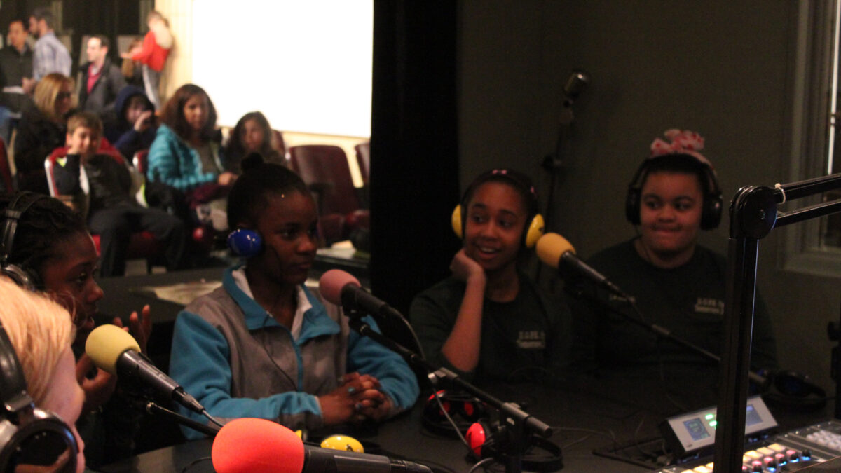 Four youth wearing headphones speaking into microphones in a radio studio