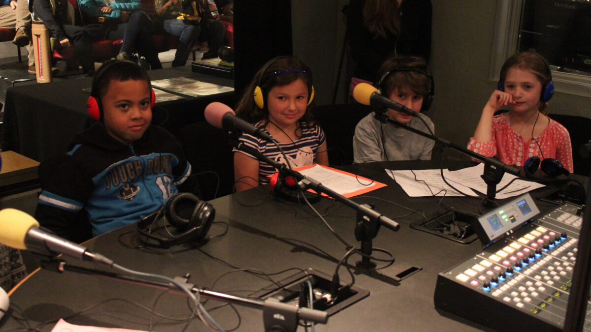 IMG_8461_wp Four youth wearing headphones sitting behind microphones in a radio studio
