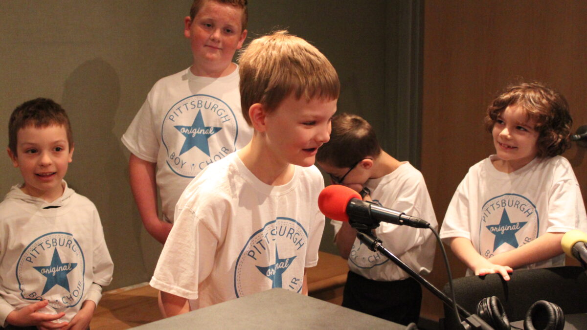 Four youth looking at another youth speaking into a microphone in a radio studio