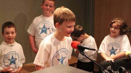 Four youth looking at another youth speaking into a microphone in a radio studio