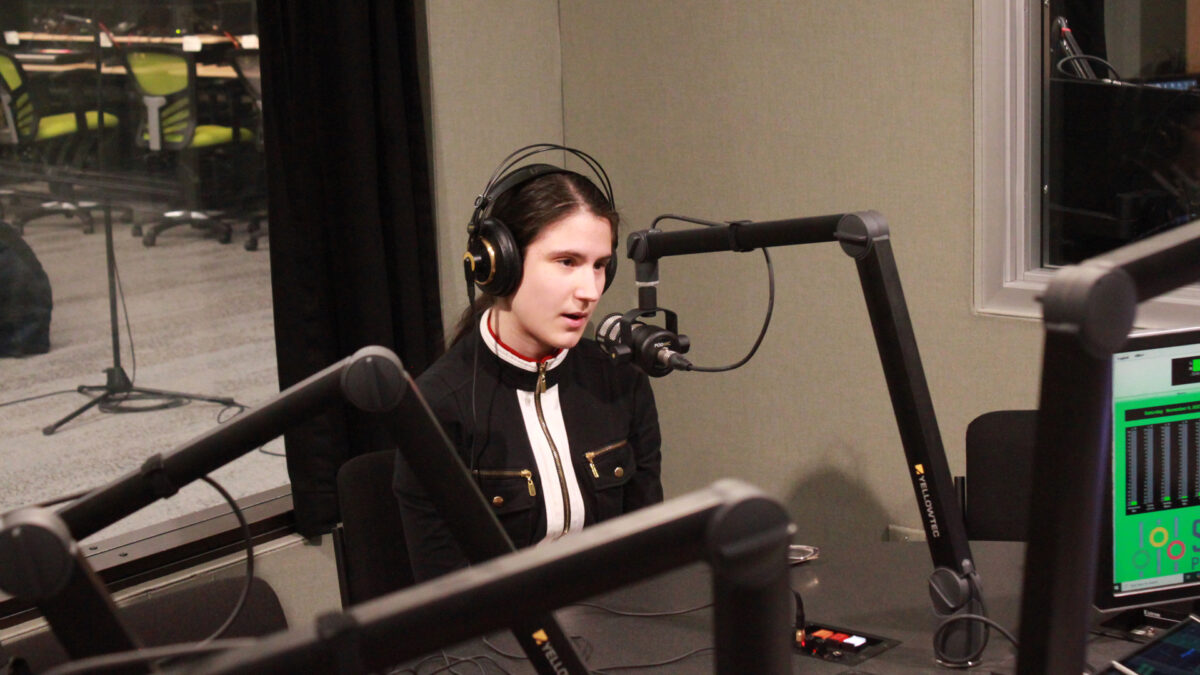 A teen wearing headphones speaking into a microphone in a radio studio