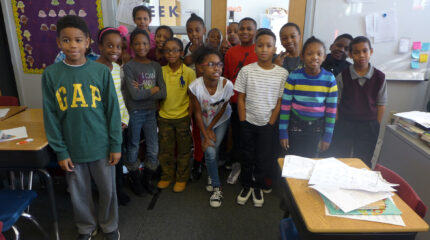 Sixteen youth smiling and standing in a classroom