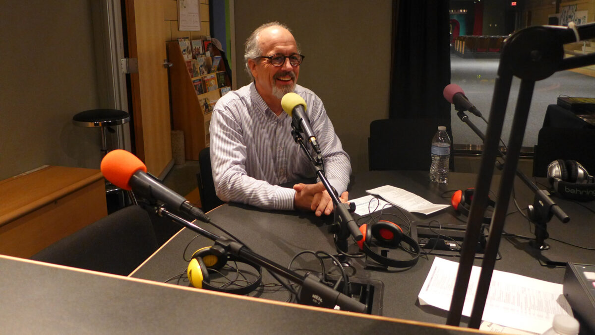 An adult smiling while speaking into a microphone in a radio studio