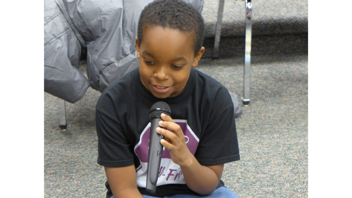 A youth sitting while holding and speaking into a microphone