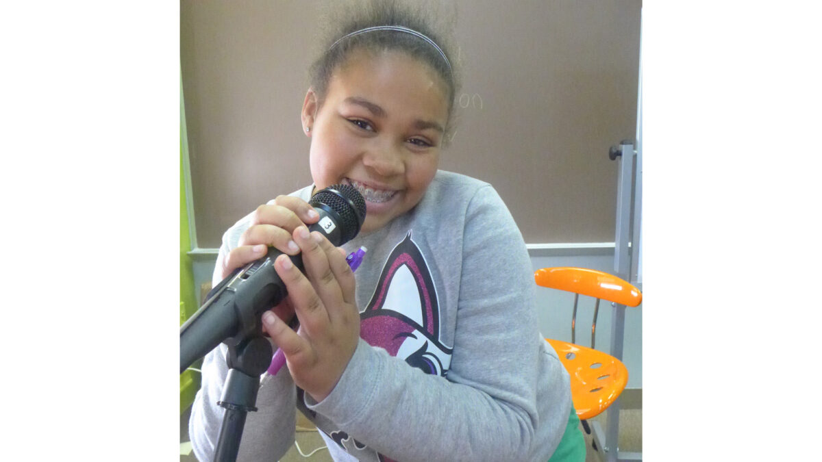A youth smiling while holding a microphone in a classroom