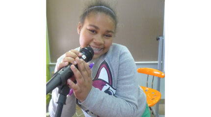 A youth smiling while holding a microphone in a classroom