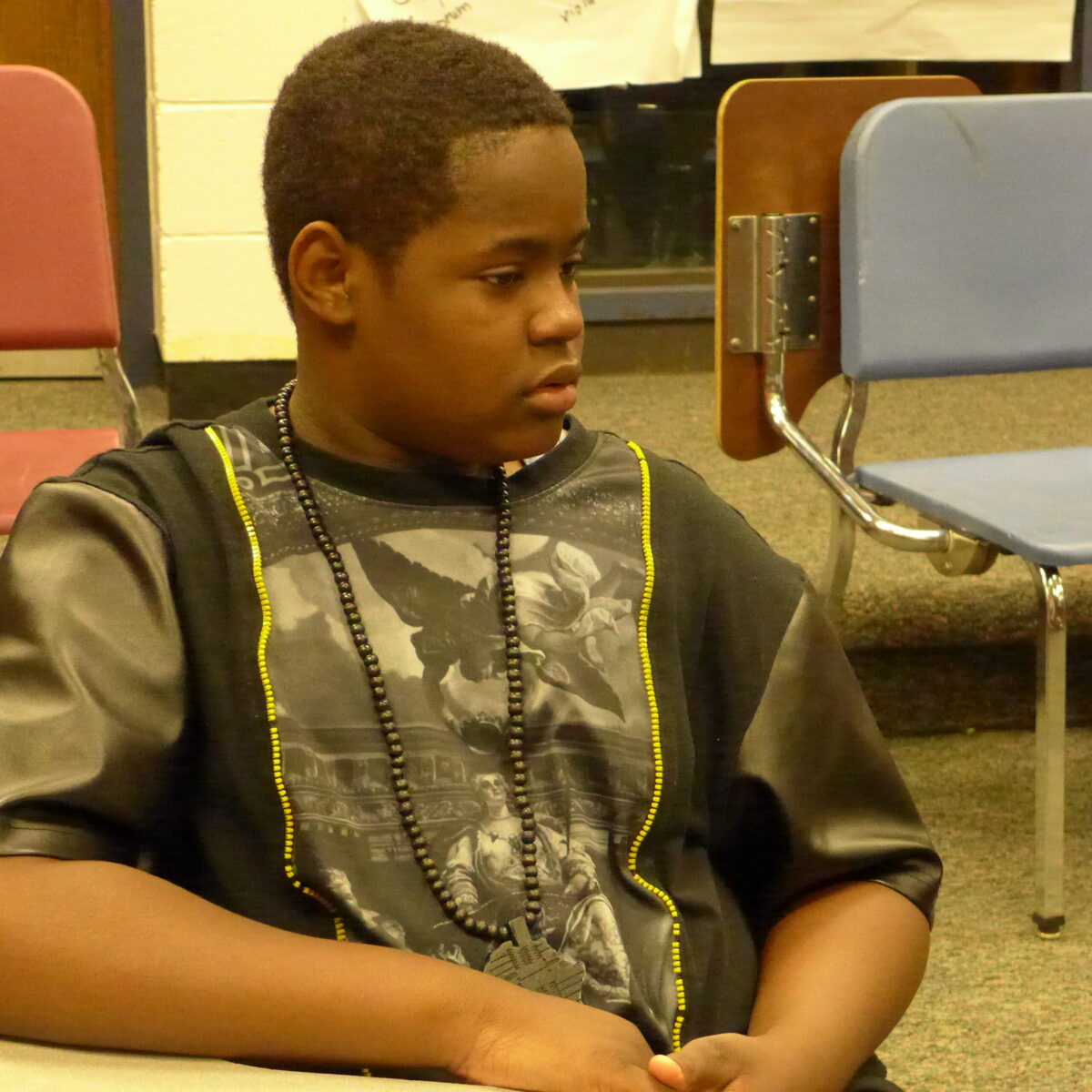 A youth looking to the right sitting at a classroom desk