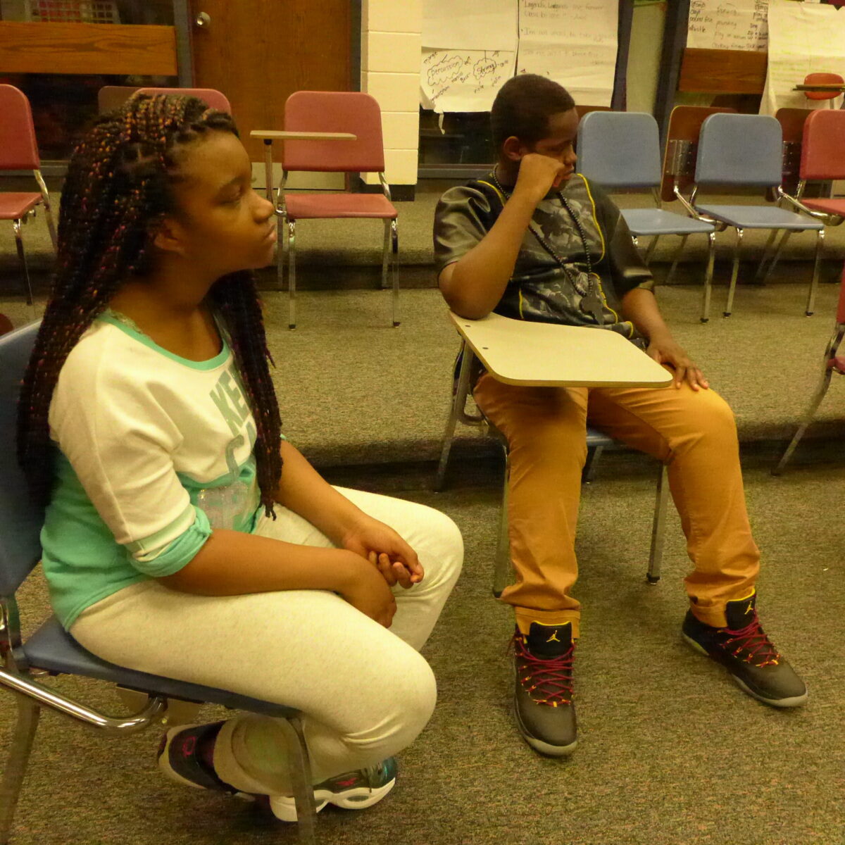 Two youth looking to the right sitting on classroom chairs