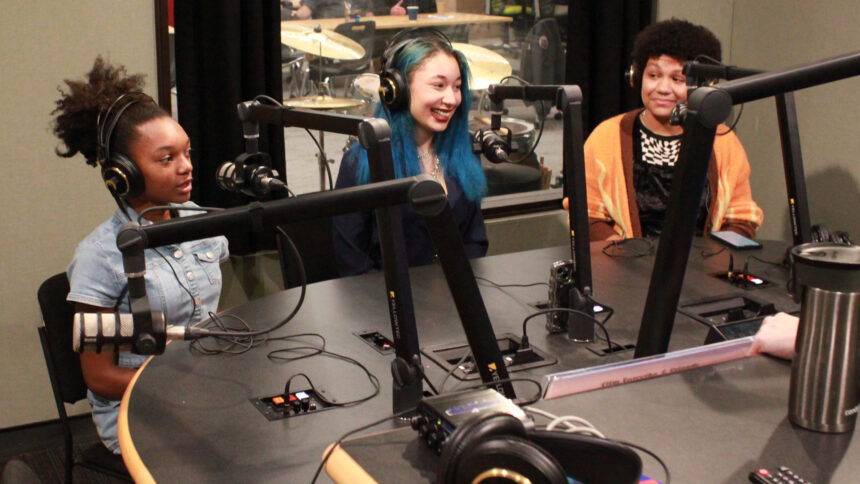 Two teens and an adult wearing headphones speaking into microphones in a radio studio