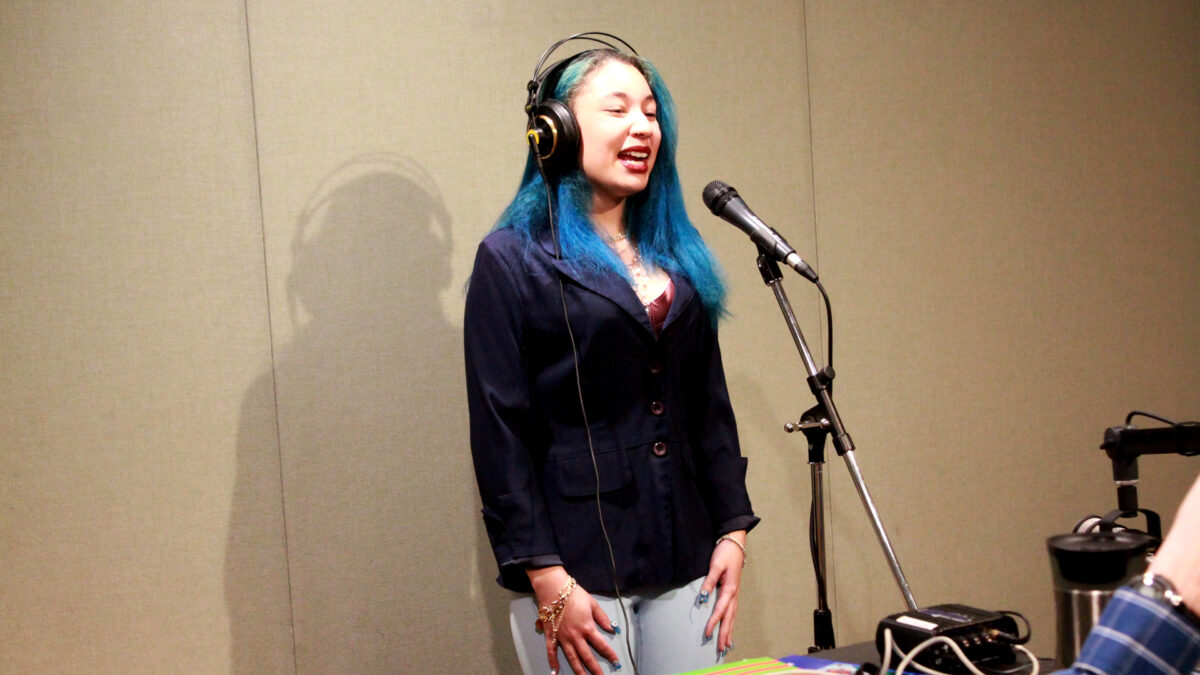 Songs-In-Our-Key-2 A teen wearing headphones singing into a microphone in a radio studio