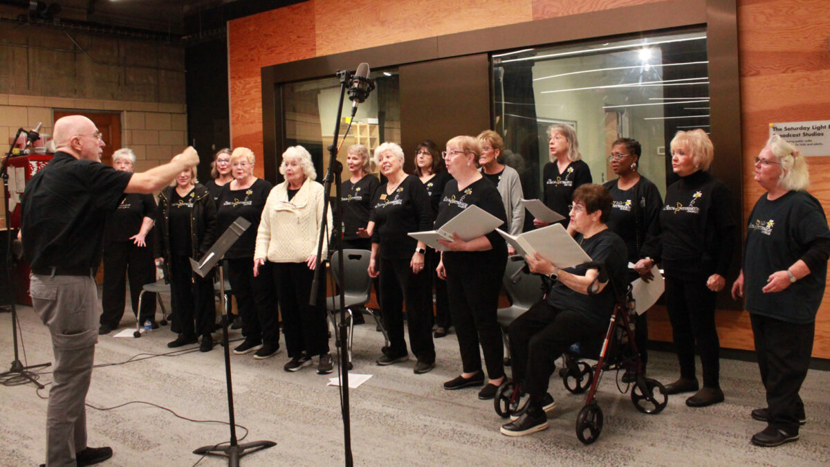 An adult conducting a group of fifteen adults singing in a choir