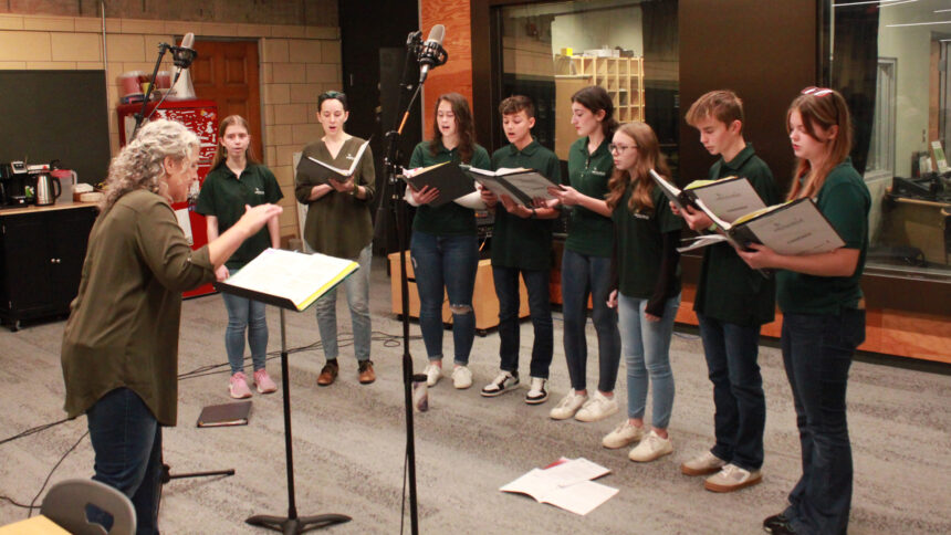 An adult conducting seven teens and an adult singing in a choir while holding binders