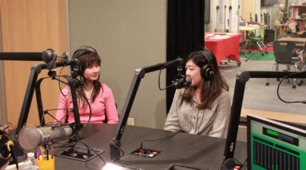 Two teens wearing headphones speaking into microphones in a radio studio