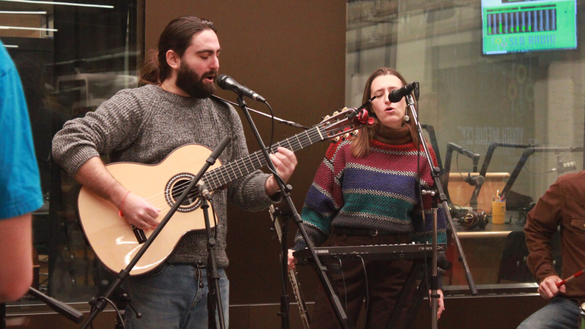 Ari-and-the-Buffalo-Kings-3 An adult playing acoustic guitar and singing into a microphone and an adult holding a flute and singing into a microphone