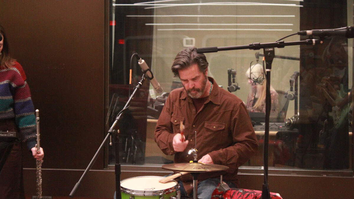 Ari-and-the-Buffalo-Kings-4 An adult playing a small drum set sitting behind a microphone