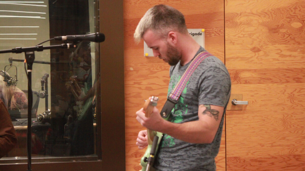 Ari-and-the-Buffalo-Kings-5 An adult playing an electric guitar standing behind a microphone